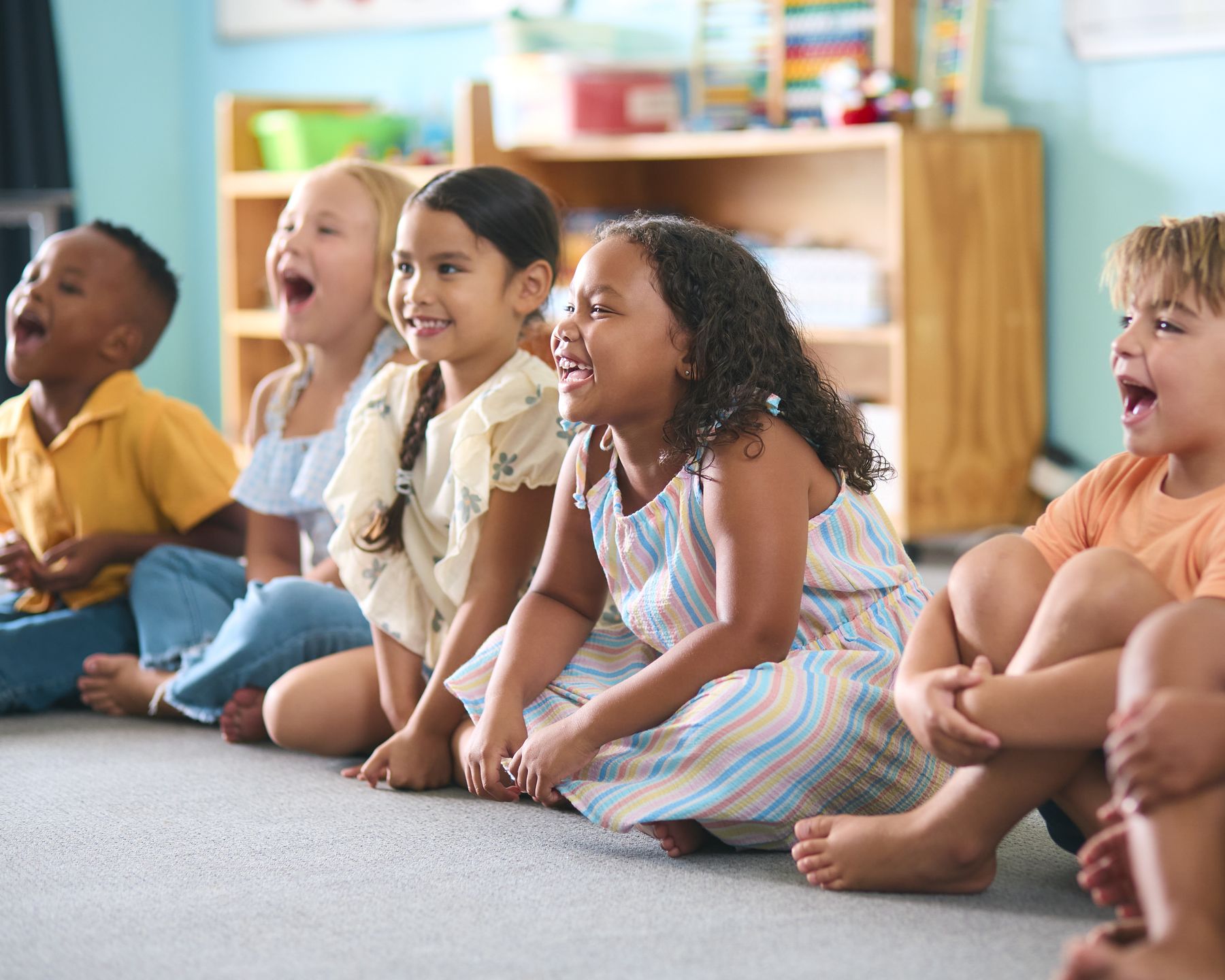 A row of preschoolers sitting on the carpet, laughing together during circle time