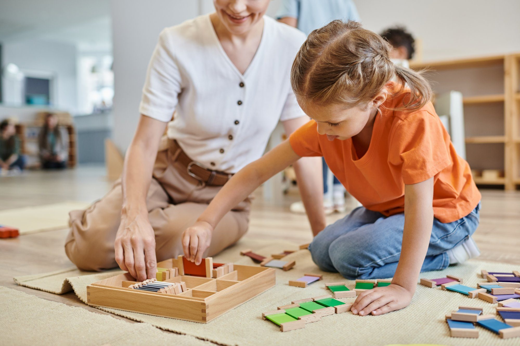 An educator and a child sort Montessori colour tablets on a floor mat