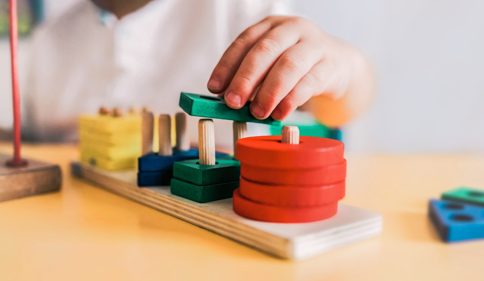 A child stacks coloured wooden shapes on a sorting board